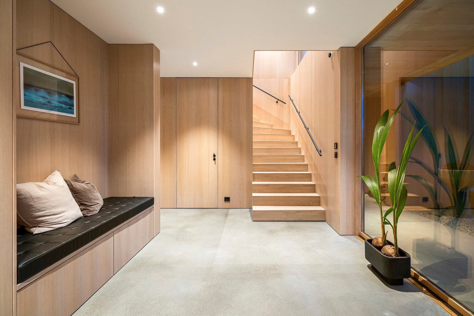 Hallen er utført med pusset betonggulv, vegger kledd i eikefiner og glatt, hvitmalt himling med downlights og et stort vindu fra gulv til tak. Galleribilde