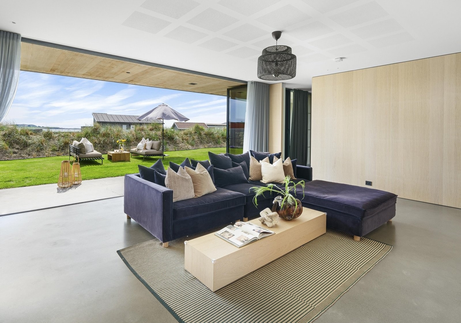 Tv-stuen har gulv i pusset betong og store foldedører i glass ut mot den overbygde terrassen, noe som helt visker ut skillet mellom ute og inne når dørene er åpne. Galleribilde