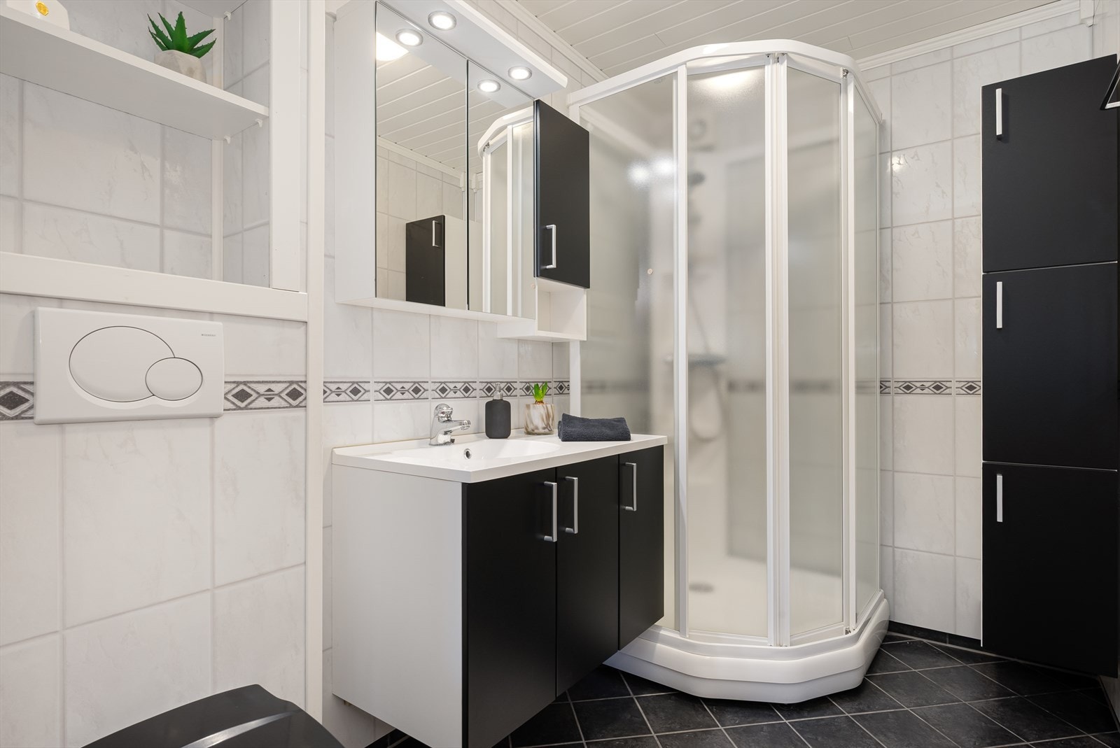 Rommet har flislagt gulv med behagelig gulvvarme og er innredet med servantskap med heldekkende servant, speilskap, overskap og vegghengt toalett. Galleribilde