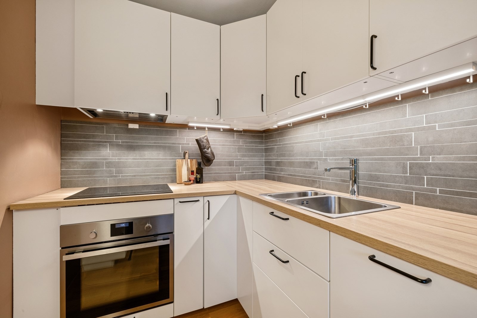 Mellom benkeplaten og overskapene er det lagt fliser som både beskytter og gir et eksklusivt løft til helheten. Praktisk benkebelysning sørger for godt arbeidslys og en hyggelig atmosfære. Galleribilde