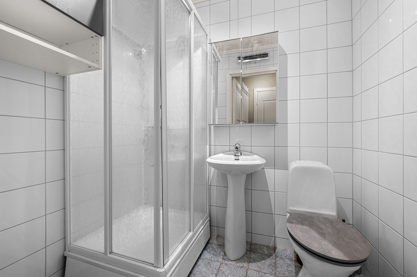 Lys flislagt bad med dusjkabinett, toalett og oppbevaringsmuligheter i skap. Felles vaskerom i 1. etasje. Galleribilde