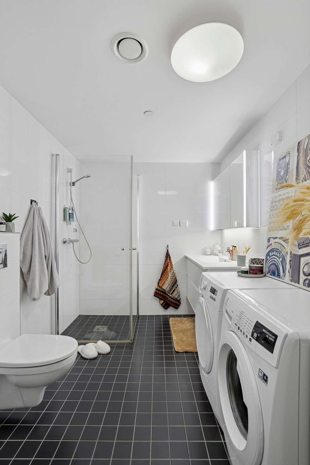 Stilrent og flislagt baderom innredet med dusjhjørne, vegghengt toalett og heldekkende servant fra 2025. Galleribilde