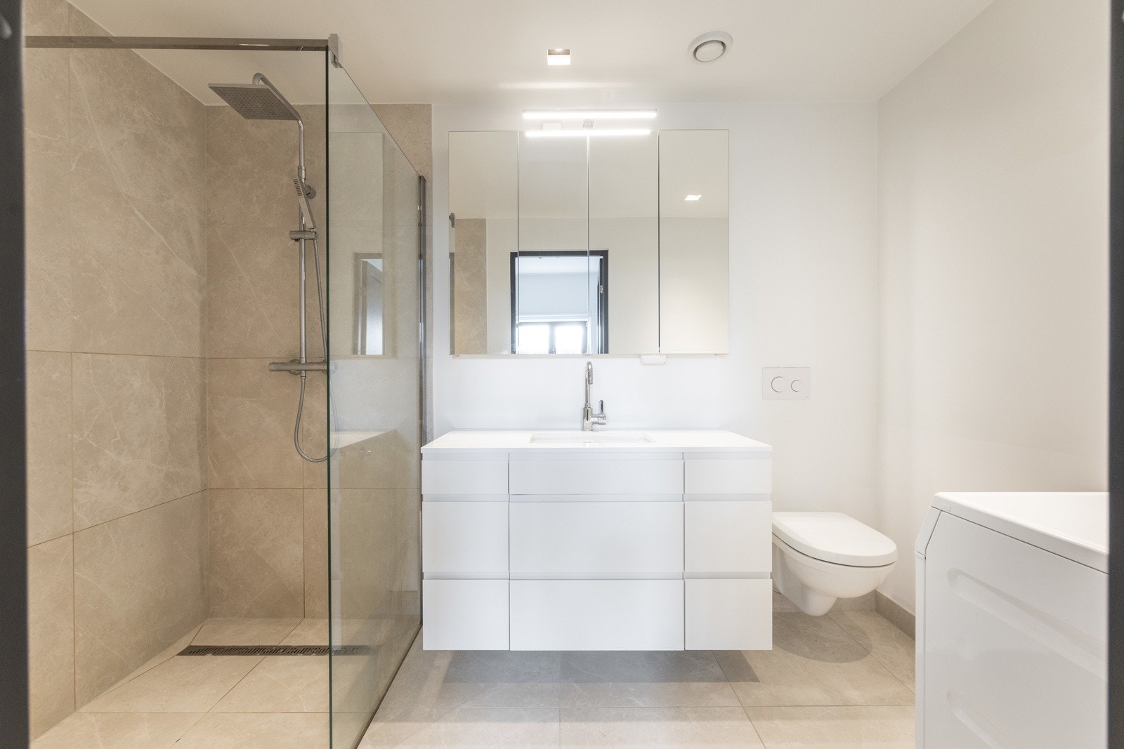 Badet er utstyrt med dusjhjørne med glassvegger, vegghengt toalett og servant med innredning og speilskap. Det er opplegg for vaskemaskin. Galleribilde