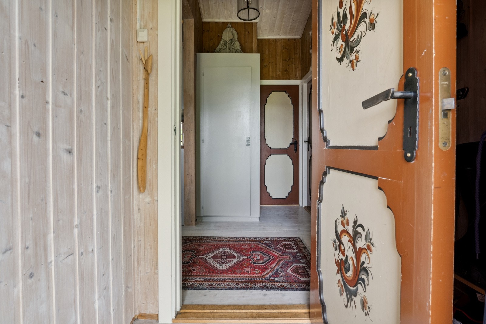 Entreen i hoveddelen har rosemalt ytterdør, lyst tregulv, lys panelhimling og mørkere vegger i panel. Galleribilde