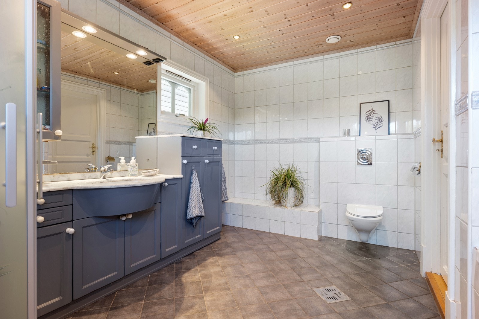 Tidløst baderom med stilren kombinasjon av grå gulvfliser med varmelkabler og hvite fliser på veggene. Galleribilde