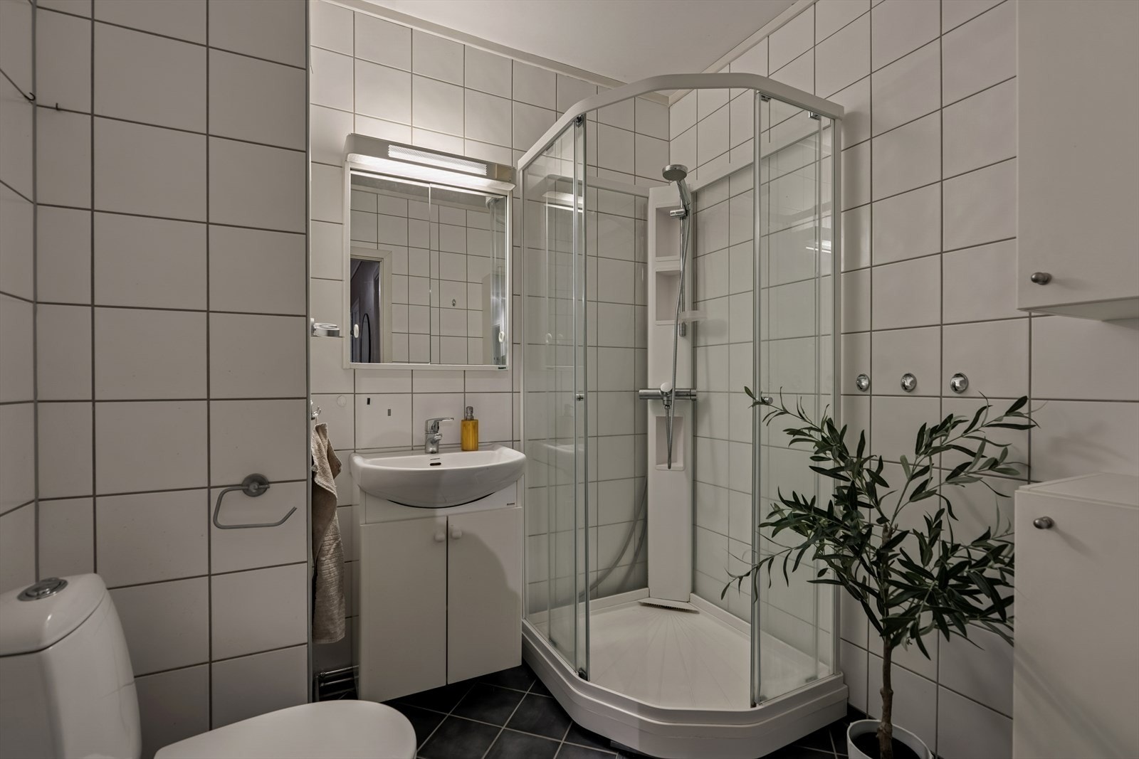 Baderom med flislagte vegger og gulv med gulvvarme. Innredet med servant med skap, gulvmontert toalett og dusjkabinett. Galleribilde