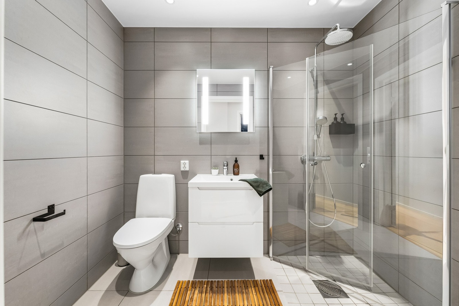 Bad i 1. etasje med flislagte flater, servantinnredning, speil med belysning og dusjnisje. Galleribilde