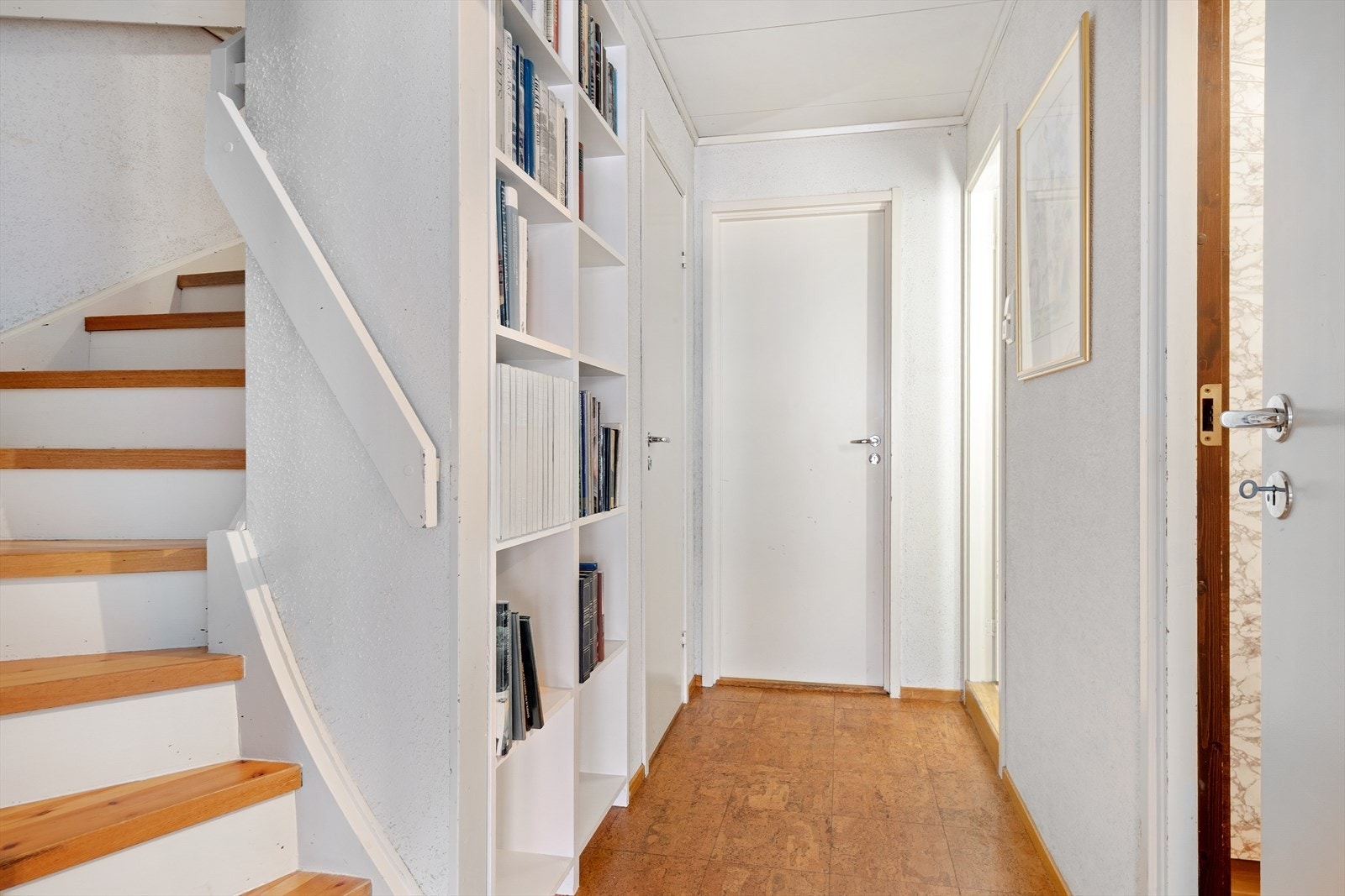 Gang i underetasje med belegg på gulv, lysmalte veggflater og integrert bokhylle Galleribilde