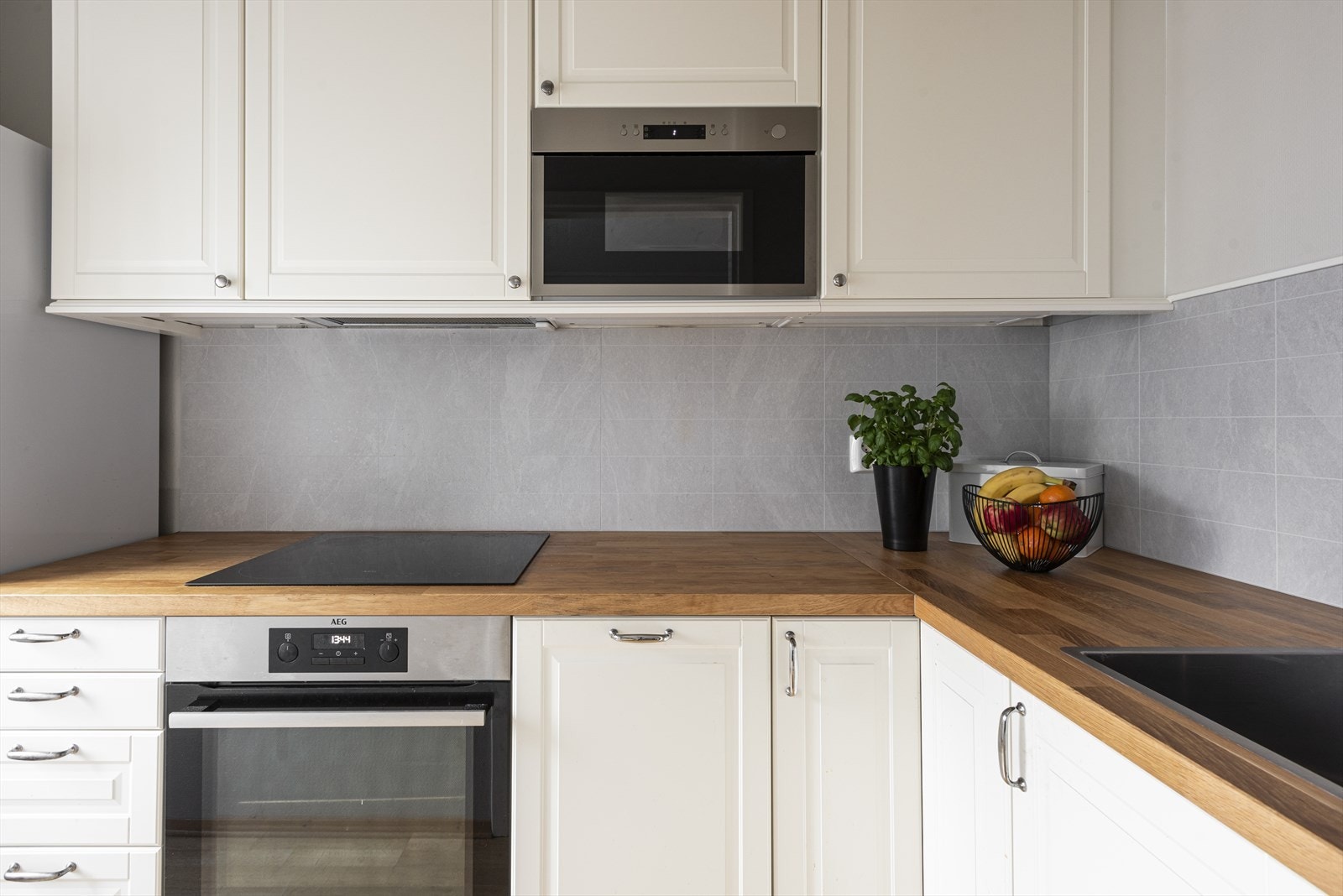 Innredning bestående av profilerte fronter og integrerte hvitevarer. Det er belysning under overskap, plater på vegg og benkeplate med nedfelt kum i rustfritt stål Galleribilde