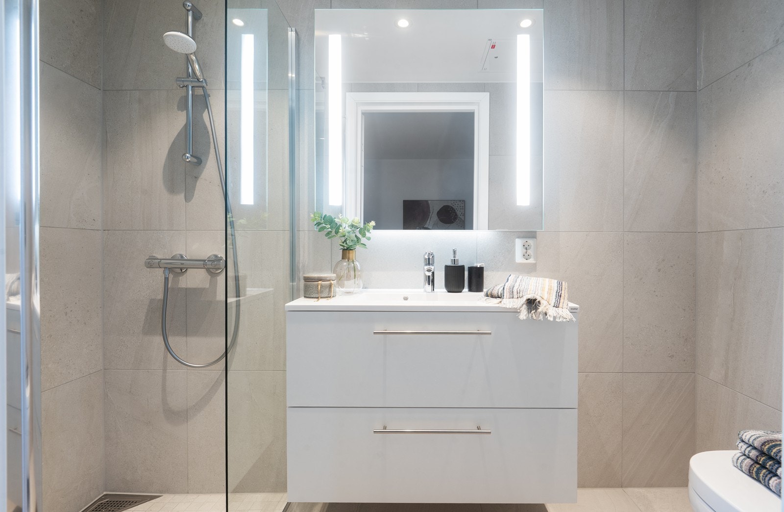 Badet er utstyrt med vegghengt toalett, dusjhjørne med glassvegger og servant med skuffeinnredning. Galleribilde