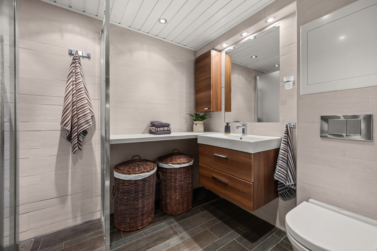 Pent flislagt bad i kjeller med varmekabler, servantseksjon med skuffer, speil og vegghengt toalett. Galleribilde