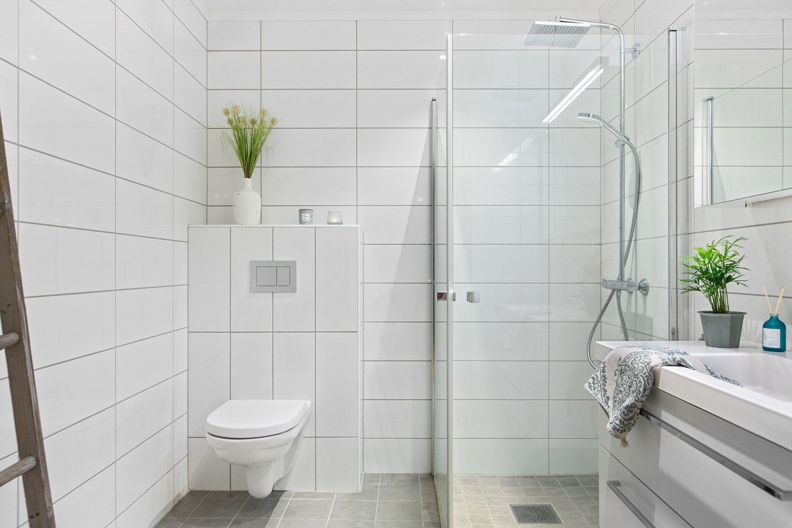 Lyse og innbydende baderom, med veggehengt toalett, dusj med glassdører og baderomsinnredning med servant, skuffer og speilskap. Galleribilde