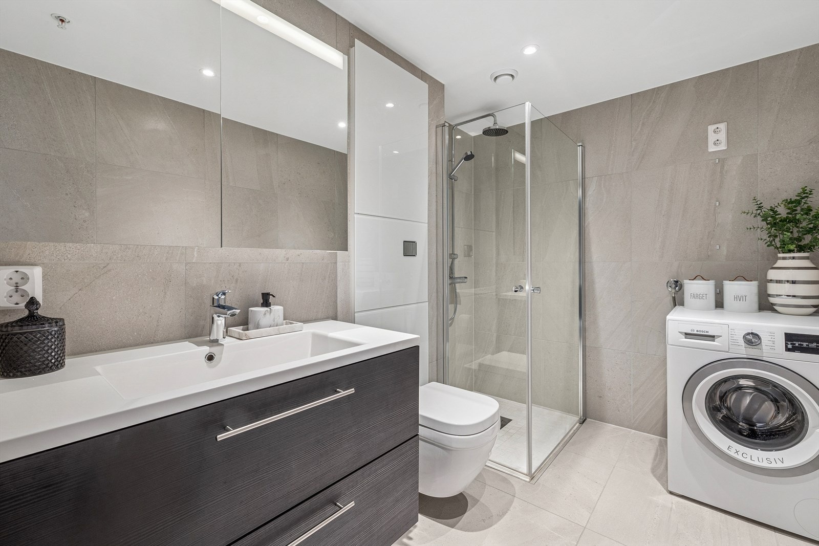 Badet er delikat innredet med store, grå fliser på gulv og vegger. I gulvet har man også vannbåren gulvvarme for ekstra komfort. Galleribilde