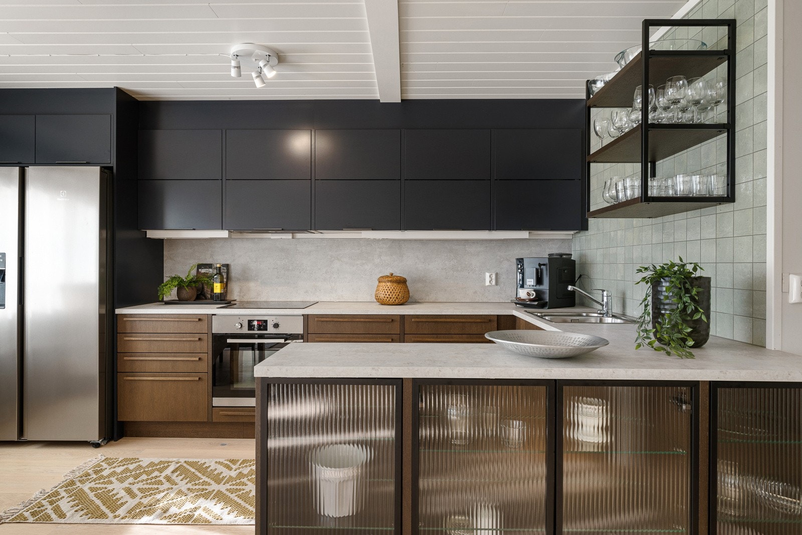 Kjøkkenet har en tidsriktig innredning fra 2025 med slette sorte overskap, underskap i treimitasjon og lys benkeplate i laminat - Mot stuen er det skap med glassfronter Galleribilde