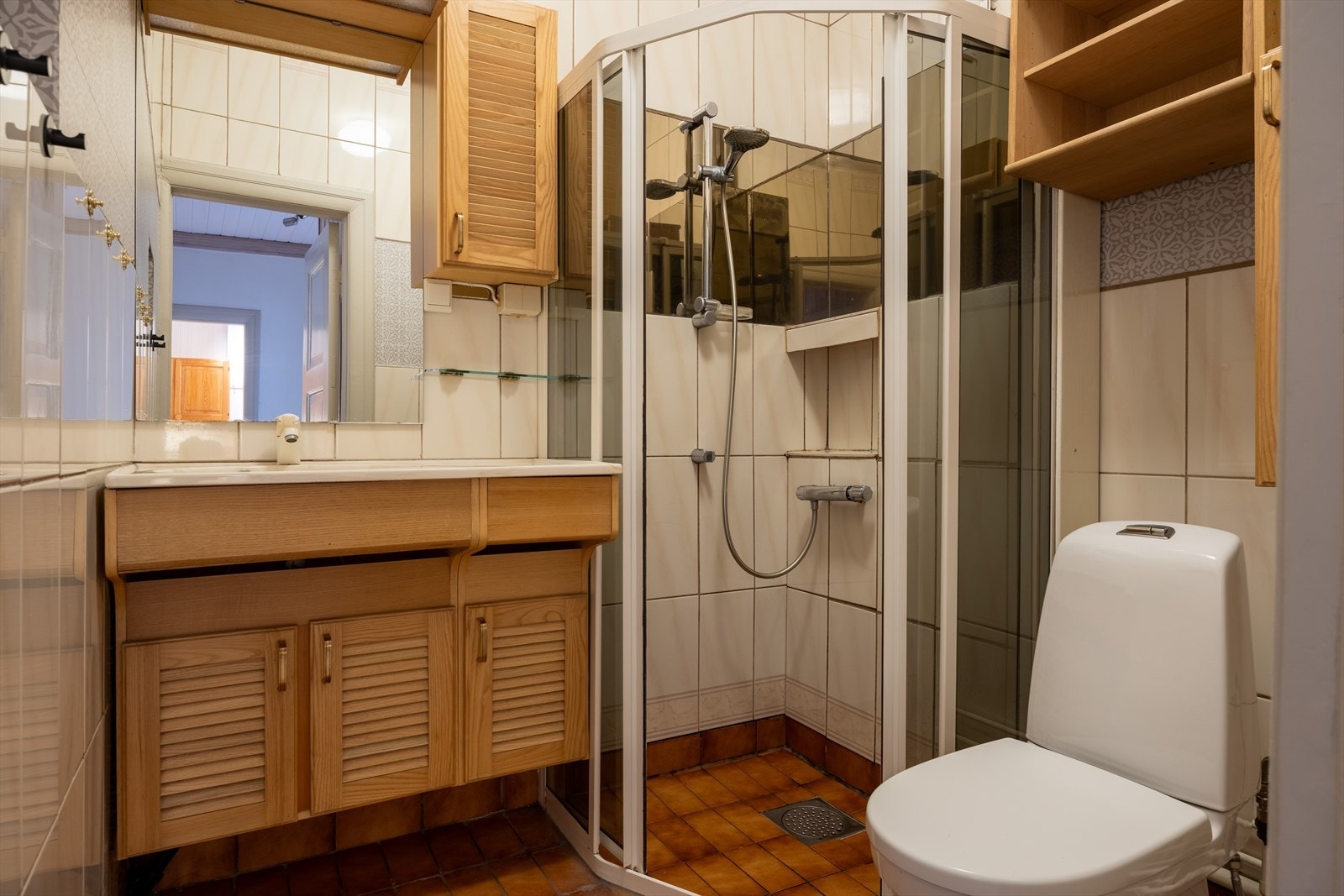 Eldre baderom med flis på gulv og flis på vegger. Malt overflate i himling. Utstyrt med dusjhjørne, innfellbare dusjdører, servant, servantskap, wc og mekanisk avtrekk Galleribilde