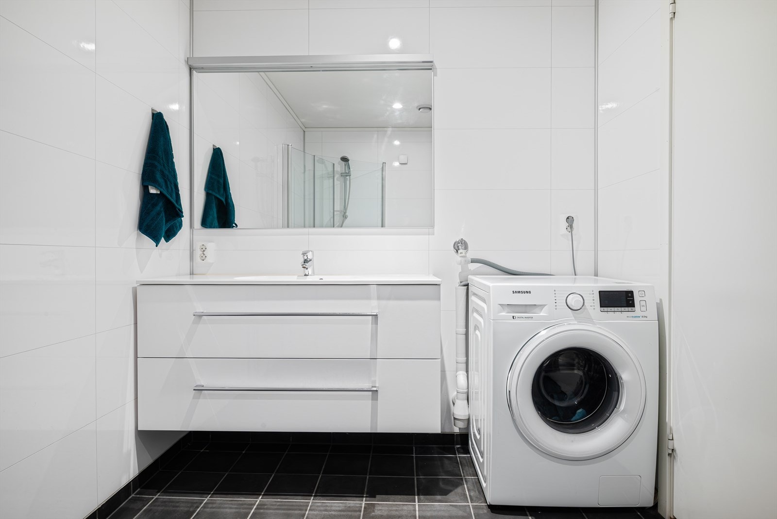 Lyst og pent baderom med varme i gulv og downlights i himling. Rommet er innredet med servant med servantskap, innsvingbare dusjdører, vegghengt toalett og opplegg for vaskemaskin. Galleribilde