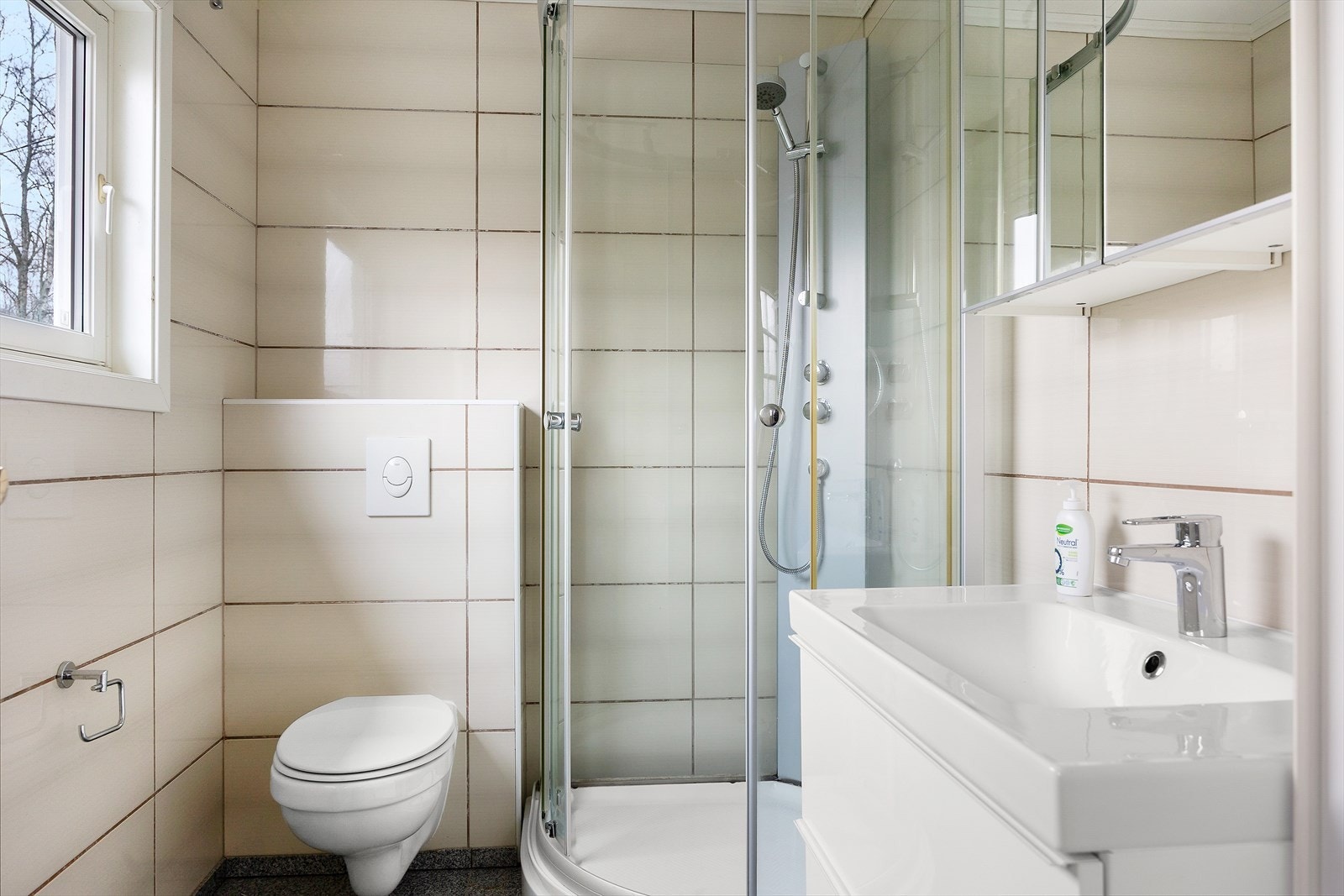 Lyst og flislagt bad. Badet er utstyrt med innredning som inkluderer servant med benkeskap, veggskap delvis med speilfronter, vegghengt toalett og dusjkabinett. Galleribilde