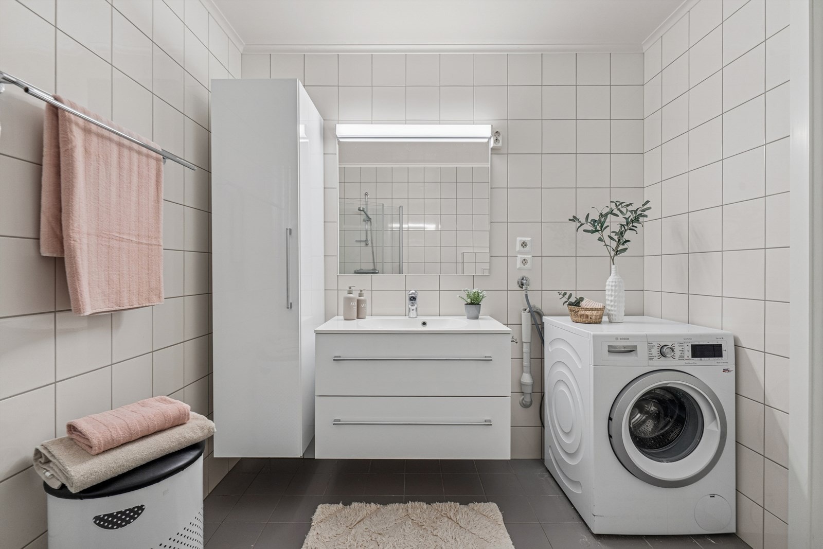 Badet fremstår som praktisk og velholdt, med fliser på både vegger og gulv som gir et rent og tidløst uttrykk. Himlingen har malte plater, og rommet er utstyrt med dusjhjørne, vegghengt toalett og servant med skapinnredning som gir god oppbevaringsplass. Galleribilde