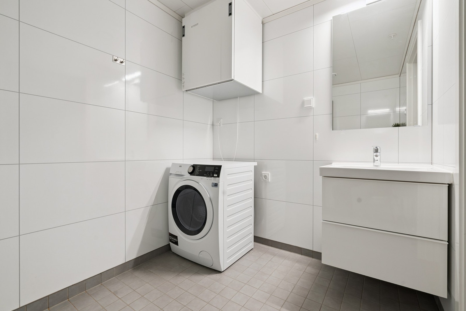 Badet er utstyrt med vegghengt toalett, dusjhjørnet, servant på møbel og opplegg for vaskemaskin. Galleribilde