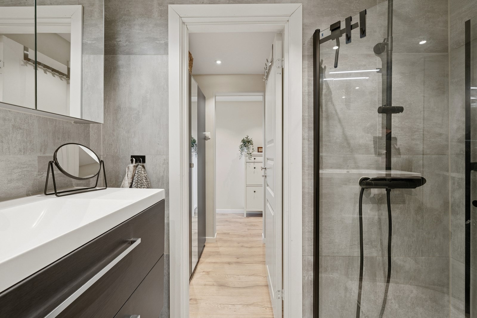 Badet er innredet med servantskap med ett-greps blandebatteri, speilskap med speilbelysning, avskjermet dusjhjørne med glass, blandebatteri og dusjgarnityr. Galleribilde