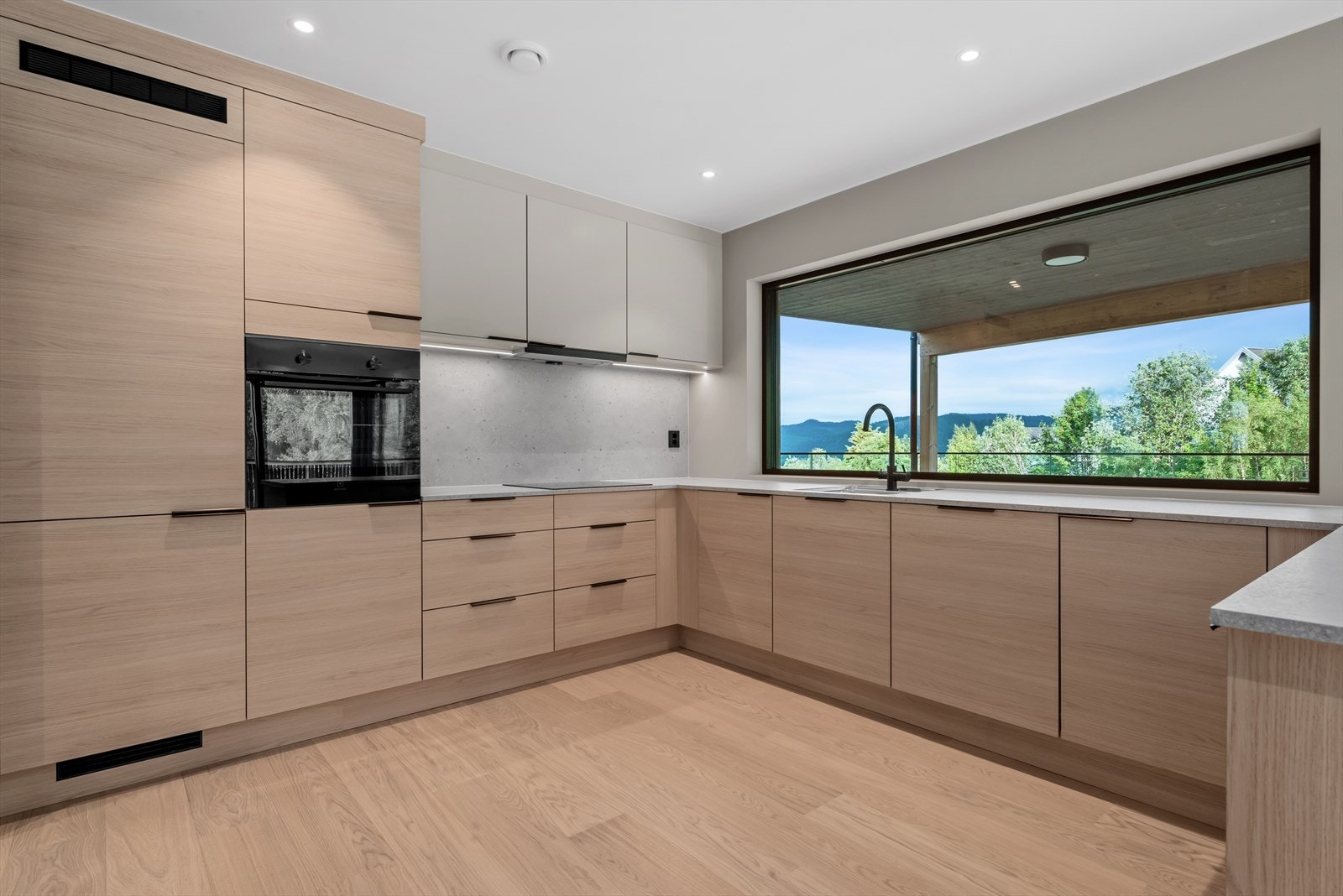 Kjøkkeninnredning med glatte fronter og integrerte hvitevarer. Mekanisk avtrekksvifte over stekesonen Galleribilde