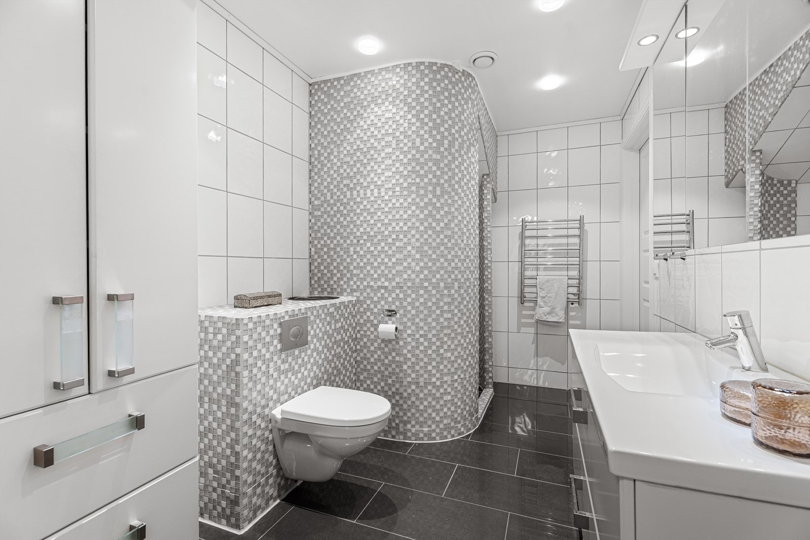 Lekkert flislagt bad i 1. etasje med gulvvarme, åpen dusjnisje, innredning med servant og vegghengt toalett. Galleribilde