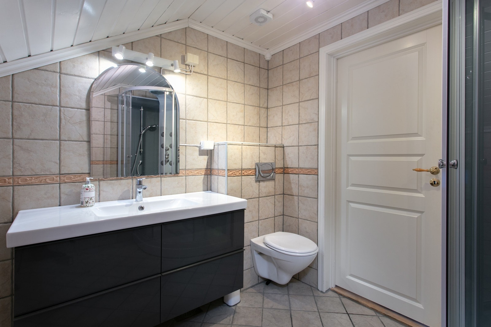 Sort baderomsinnredning med skuffer og ovenpåliggende servant med ett-greps armatur. Speil med overlys og stikkontakt over servant. Galleribilde