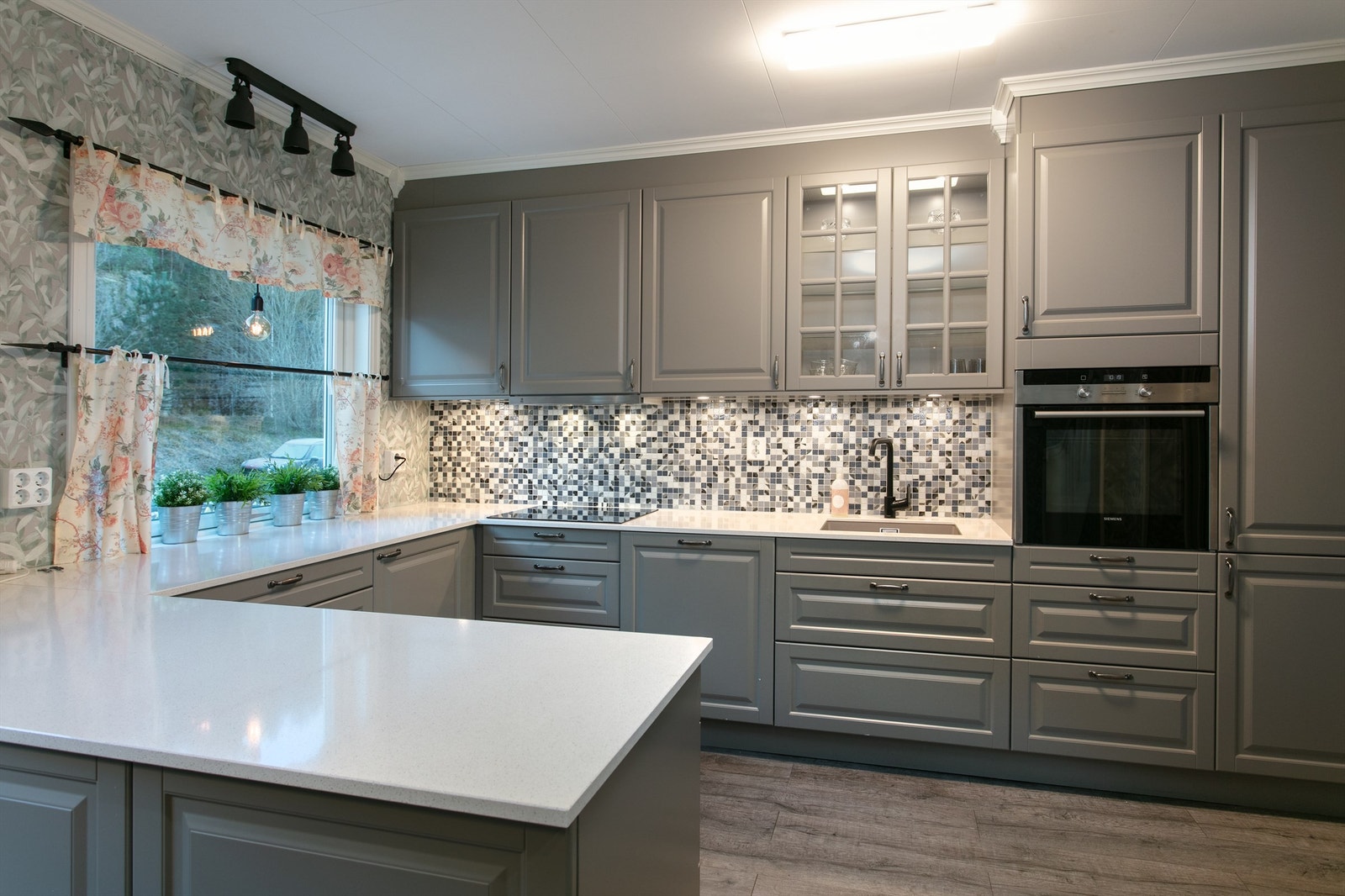 Kjøkkeninnredning med profilerte fronter og benkeplate av stein. Det er kjøleskap, fryseskap, oppvaskmaskin, platetopp, stekeovn og vannstoppsystem. Galleribilde