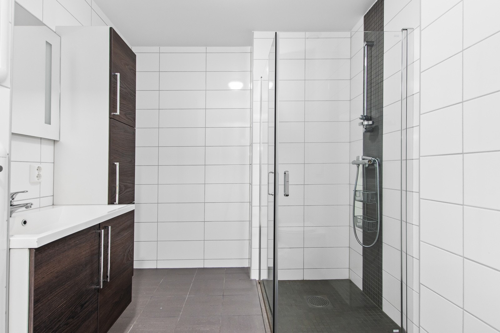 Fint flislagt bad med varmekabler i gulv, servant, dusjhjørne, høyskap, klosett og opplegg for vaskemaskin. Galleribilde