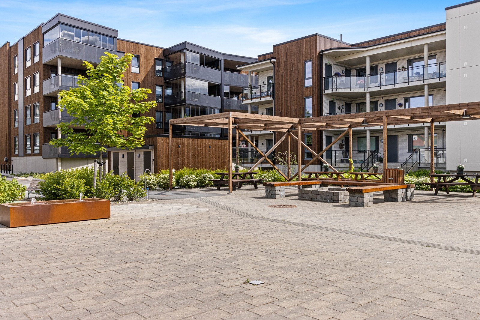 Belegningsstein, sittebenker, diverse beplantning, vannfontene, felles grillplass, belysning og "paviljoner". Galleribilde