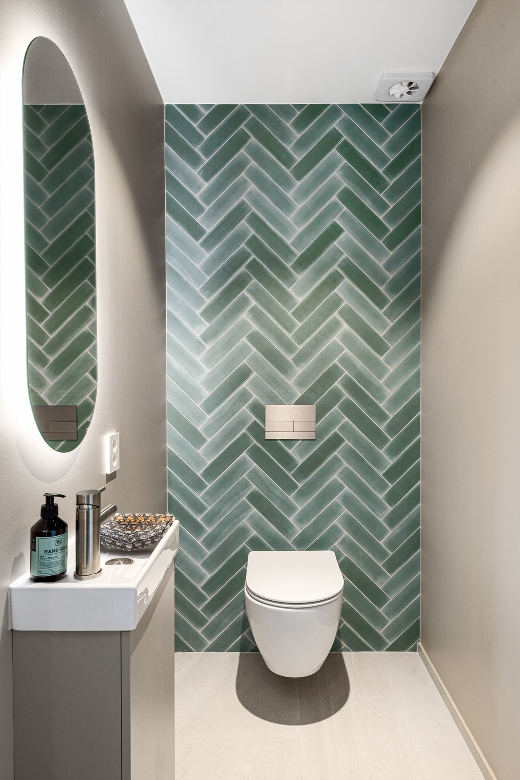 Toalettrommet fremstår som en liten perle i hjemmet med særdeles gjennomførte og stilfulle materialvalg. En dekorativ flisvegg skaper et blikkfang og gir rommet et eksklusivt preg. Rommet er smakfullt innredet med servant, speil og vegghengt toalett. Galleribilde