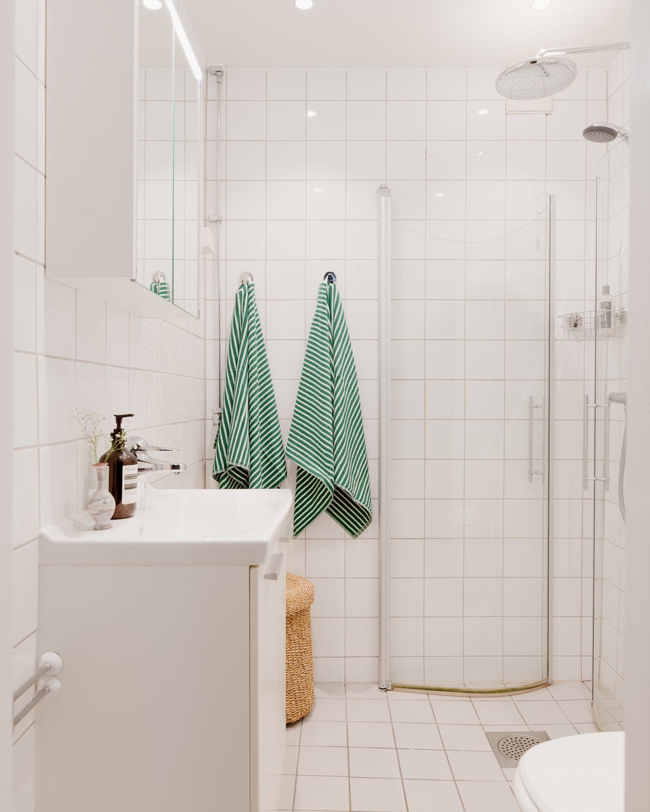 Badet fremstår med fliser, og er innredet med klosett, veggmonterte dusjdører, servant med underskap og speilskap med lys. Galleribilde