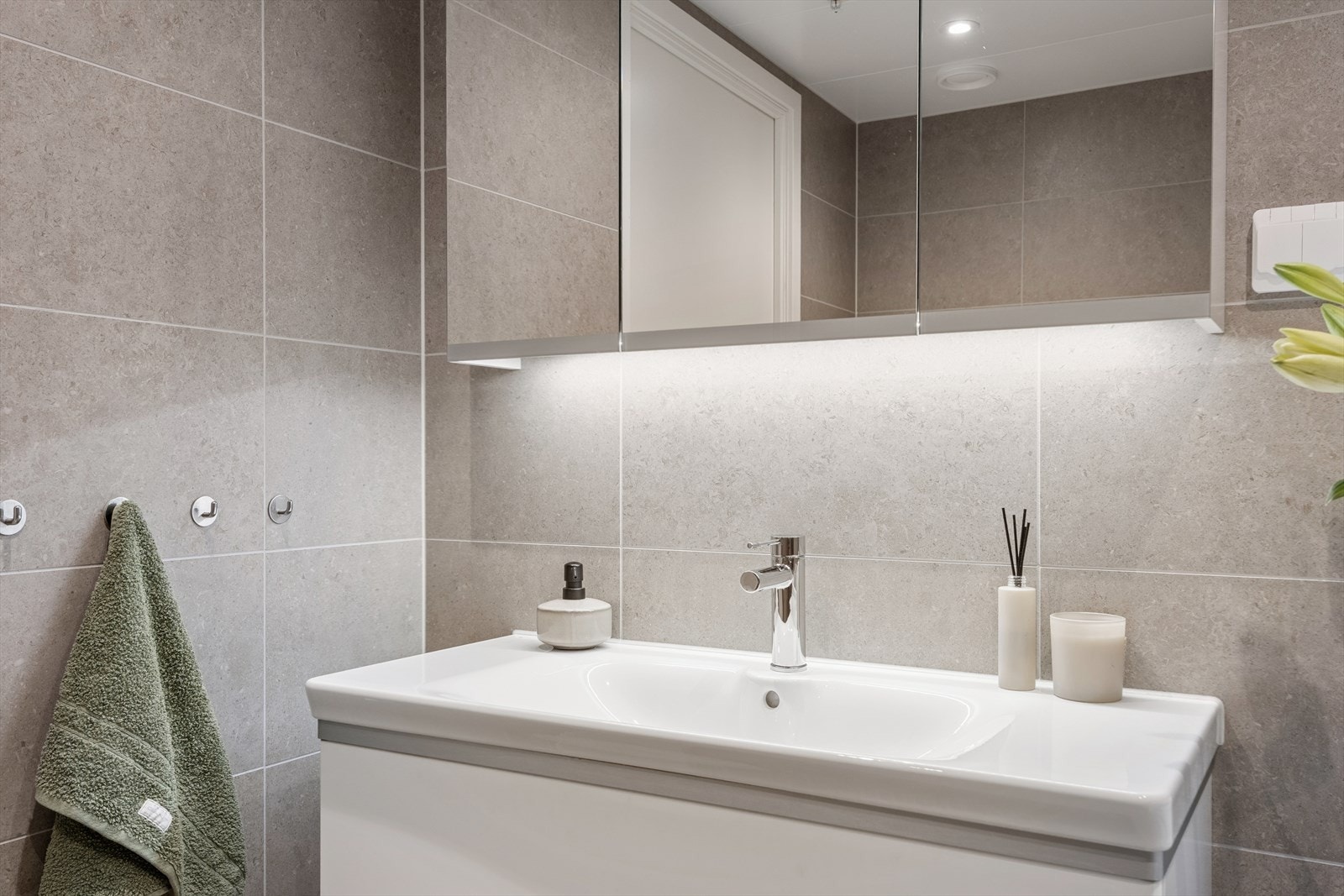 Moderne baderomsinnredning med hvitt servantskap, speilskap, vegghengt WC og dusjhjørne med svingdører. Galleribilde