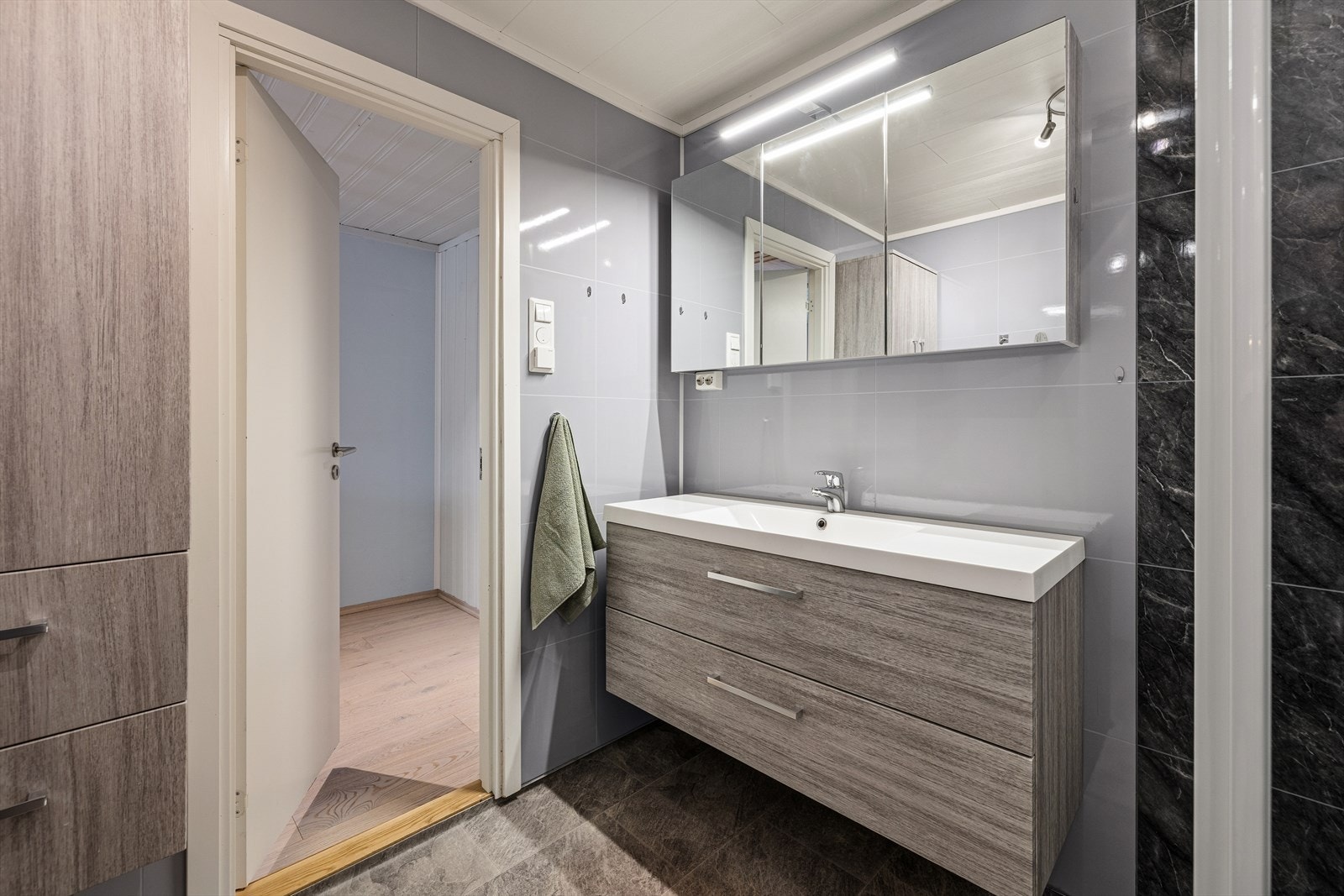 Badet har servant med underskap, speil med tilhørende belysning, dusjvegger og vegghengt wc. Galleribilde