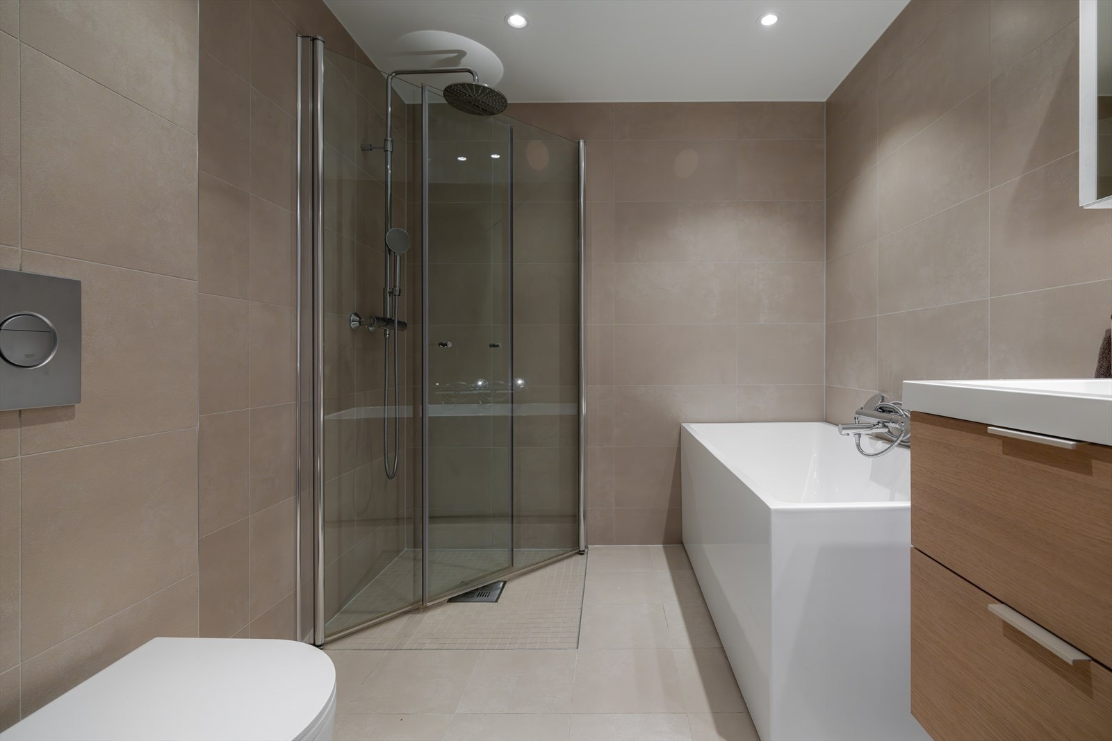 Lekkert flislagt bad fra byggeår med badekar, regnfallsdusj og moderne innredning, utført i gjennomført og stilrent design. Galleribilde