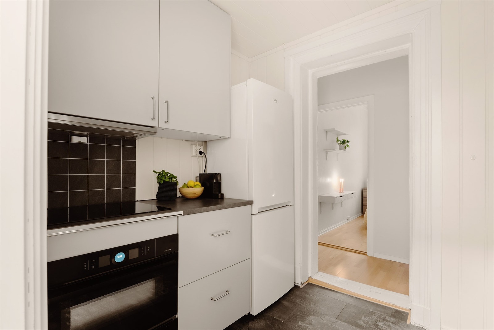 Praktisk kjøkkenrom innredet med stekeovn, platetopp, oppvaskmaskin samt frittstående kjøleskap med frysedel Galleribilde