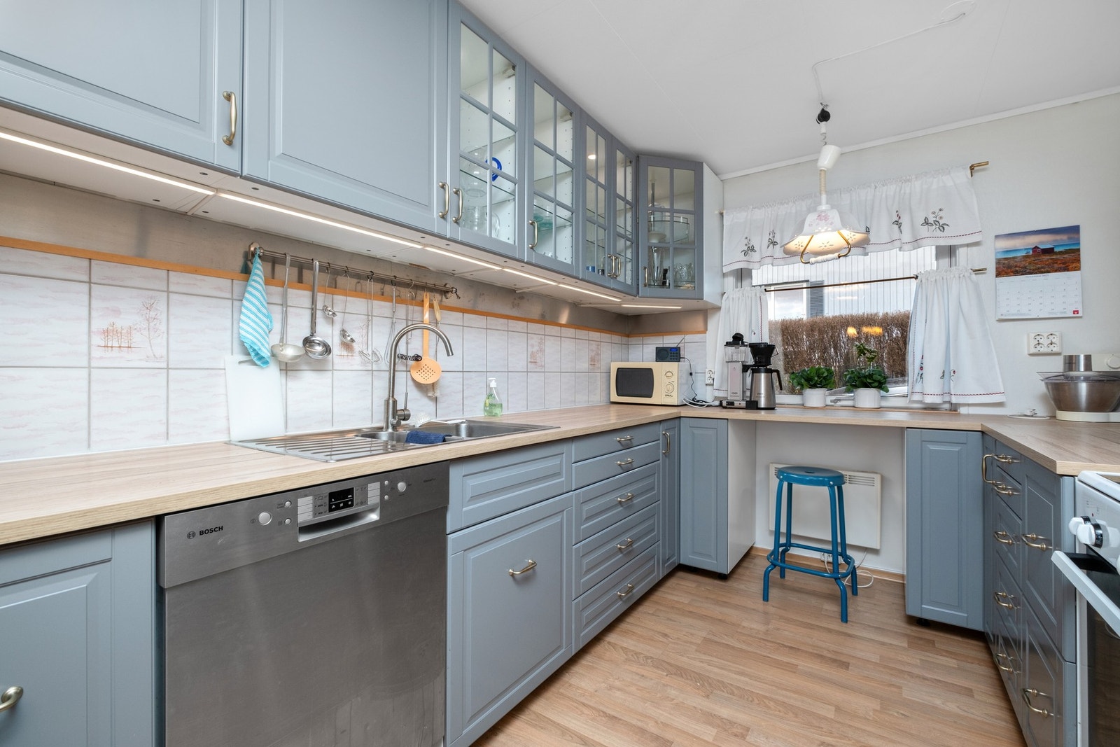 Laminat på gulv, tapet på vegg med flis over deler av benkeplate og malt overflate i himling. Galleribilde