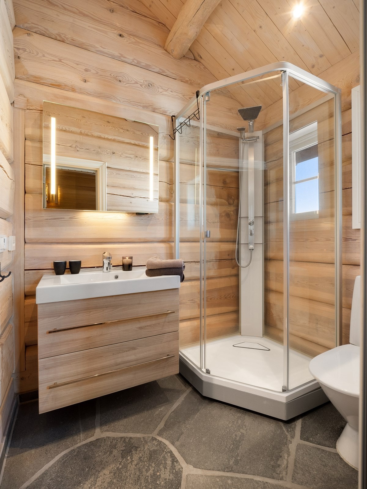 Bad med vask i seksjon, dusjkabinett og wc. Adkomst til badstue. Skifer på gulv med varmekabler under. Galleribilde