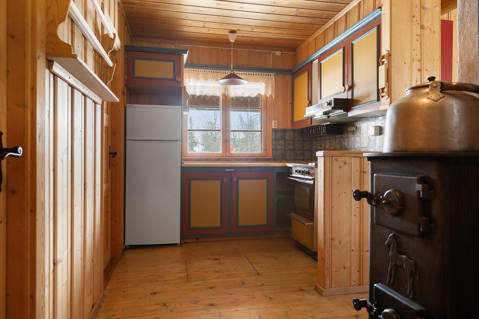 Kjøkkenet har innredning i malte plater med over-og underskap, laminat benkeplate i trefylling, samt frittstående kjøleskap, komfyr og ventilator. Galleribilde