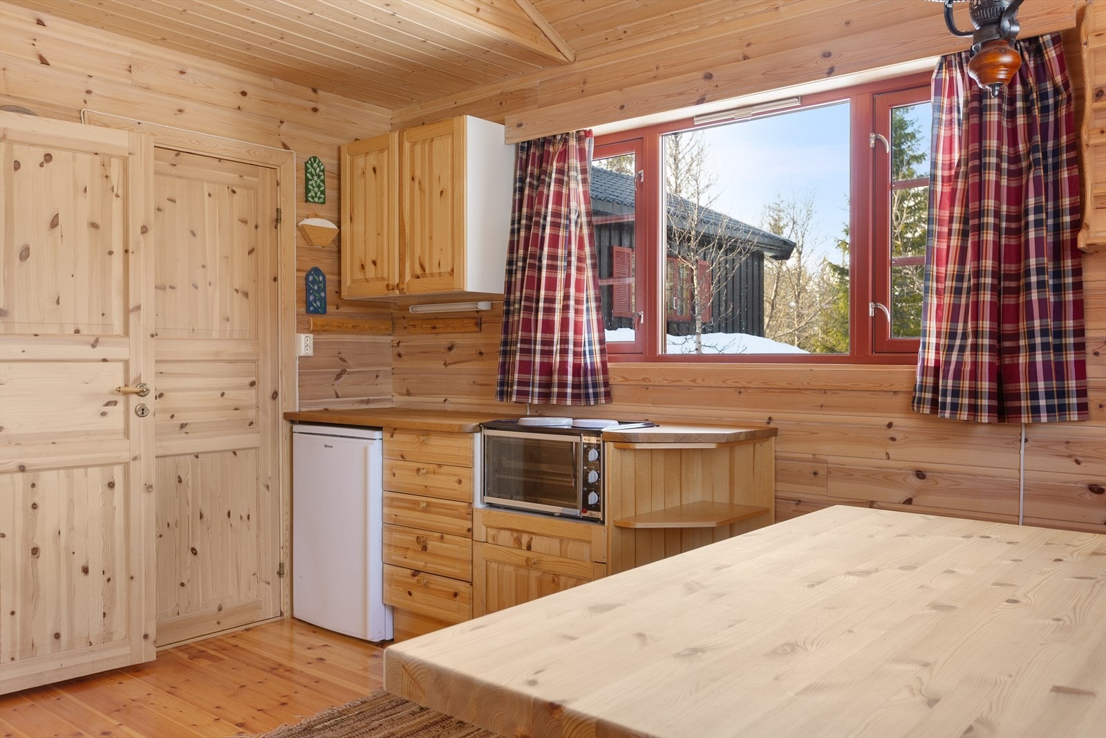 Enkel liten kjøkkeninnredning med over-og underskap i plater med profilerte heltre fronter, heltre benkeplate i eik og frittstående kjøleskap og hybelkomfyr. Galleribilde