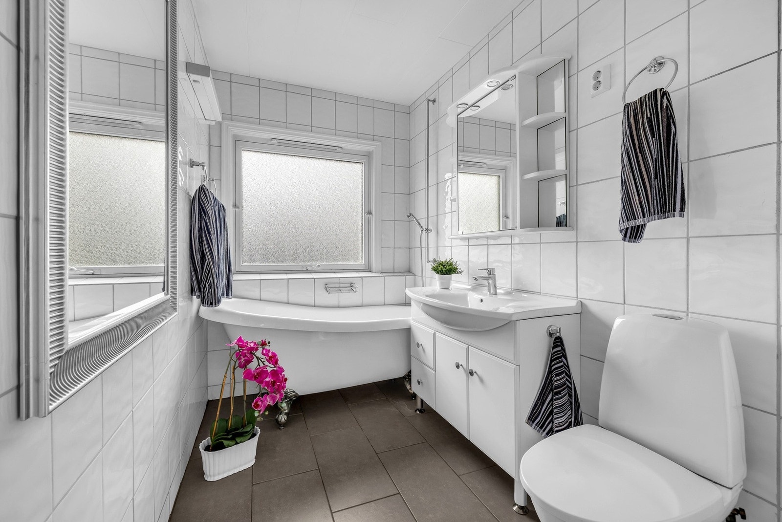 Badet har lyse fliser, stort vindu, badekar, servant med skap og speil. Galleribilde