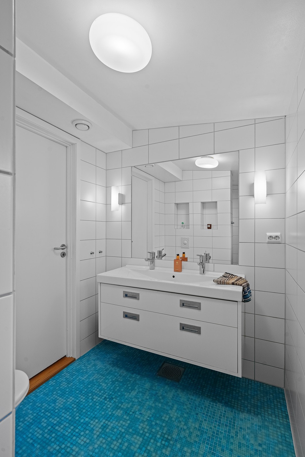 Flisebelagt baderom er innredet med vask i seksjon, vegghengt toalett og dusj. Galleribilde