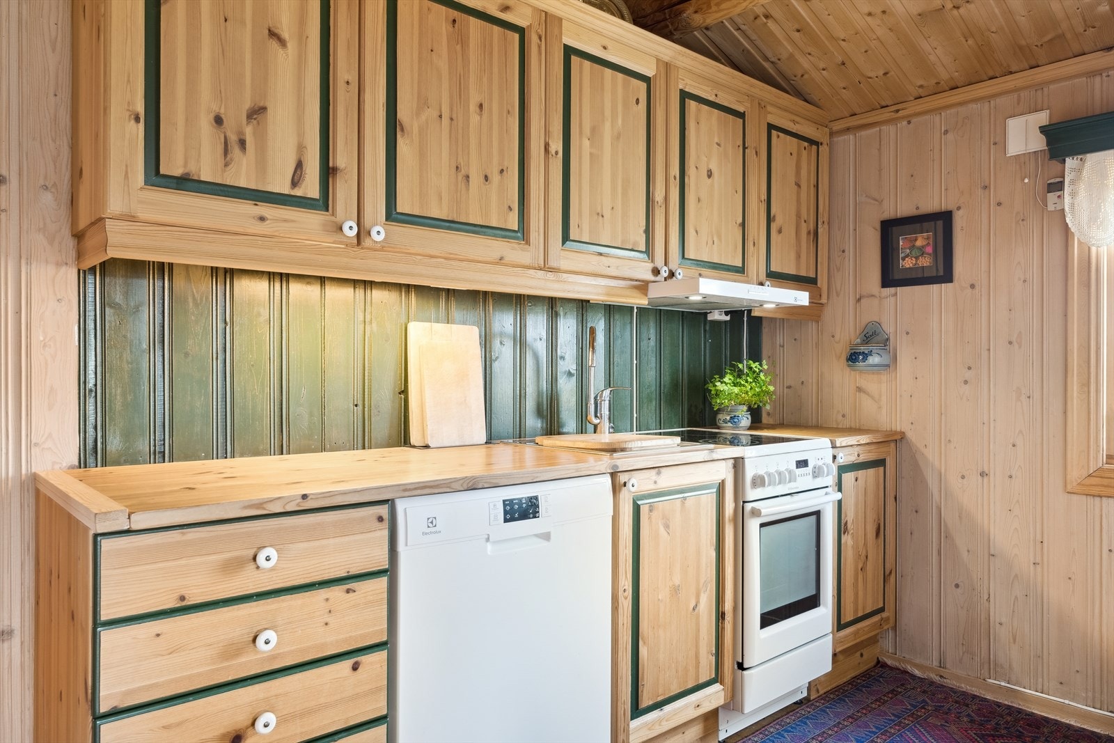 Frittstående komfyr og kjøkkenventilator med avtrekk ut. I innredningen er det også oppvaskmaskin. Galleribilde