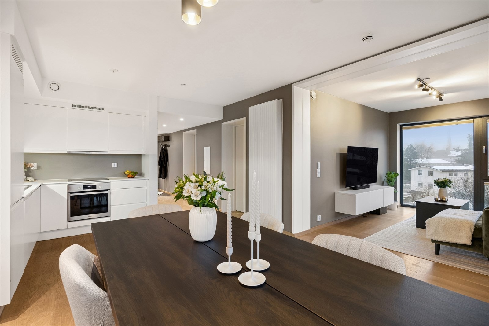 Åpen stue- og kjøkkenløsning med lys parkett og integrerte hvitevarer. Galleribilde