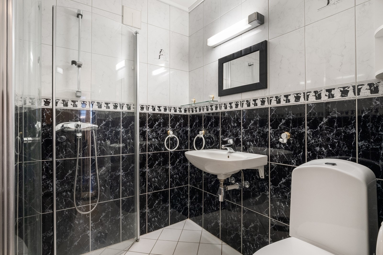 Pent flislagt bad med varmekabler i gulv. Badet er innredet med toalett, servant og dusjhjørne med innfellbare dusjdører Galleribilde