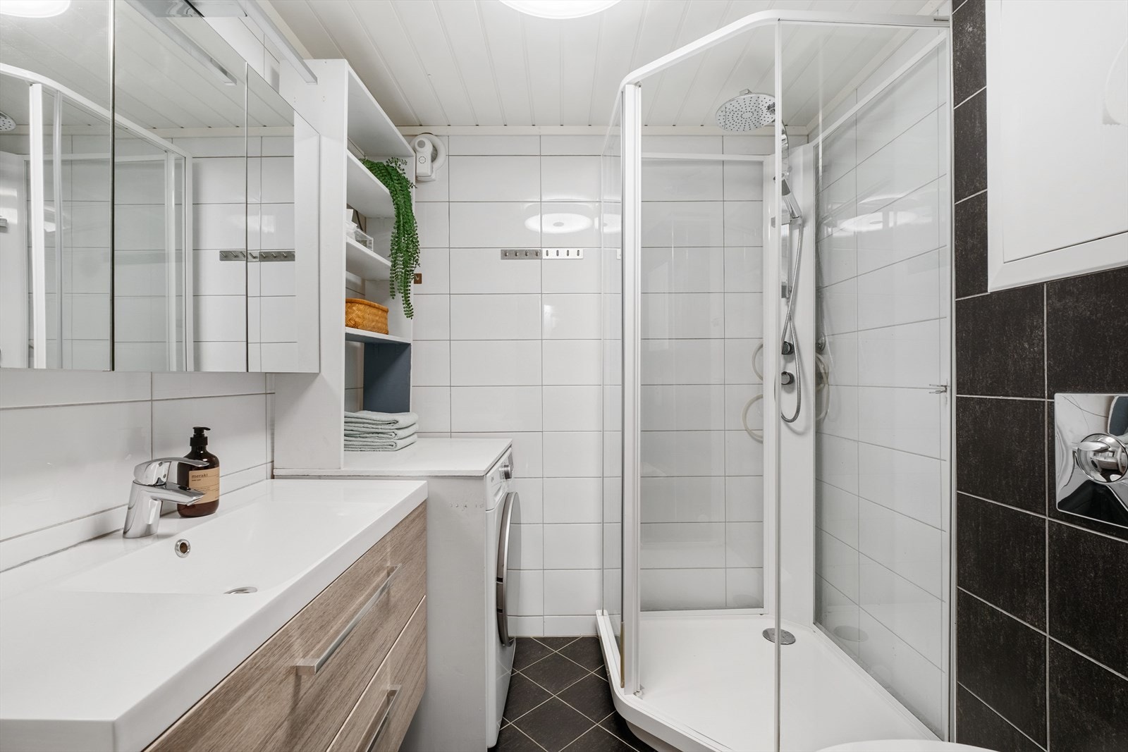 Pent flislagt bad utstyrt med dusjkabinett, vegghengt toalett og opplegg for vaskemaskin. Galleribilde