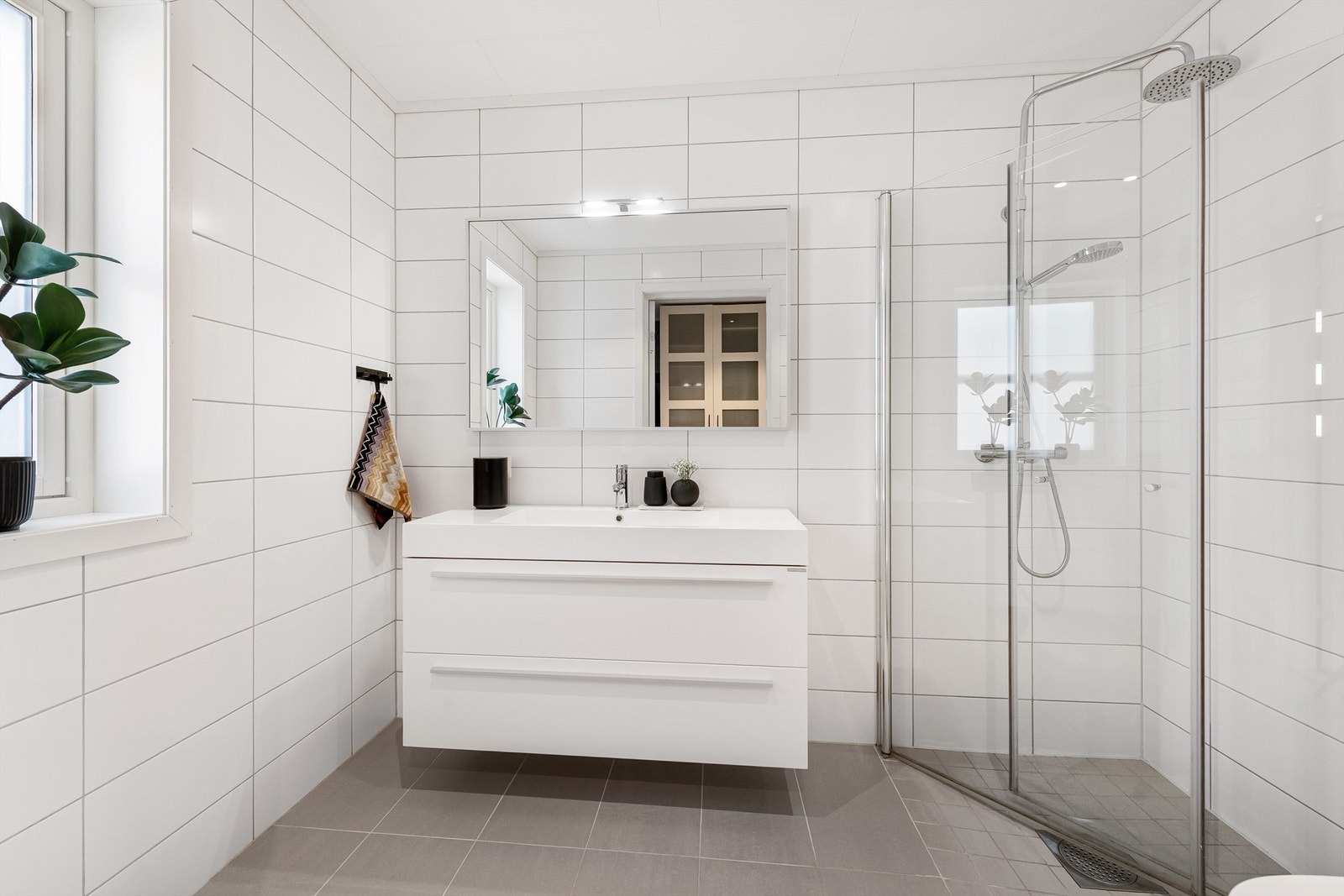 Flott flislagt bad i 1. etasje. Baderomsinnredning med skuffer og ovenpåliggende servant med ett-greps armatur. Speil med overlys og stikkontakter over servant. Galleribilde