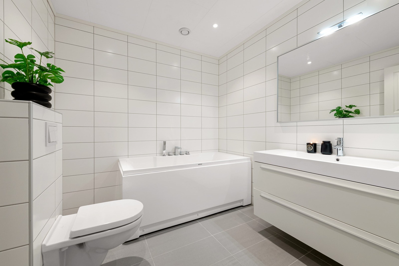 Flott flislagt bad i underetasjen med servantinnrending, speil med overlys, frittstående badekar med badekarsarmatur og vegghengt toalett Galleribilde