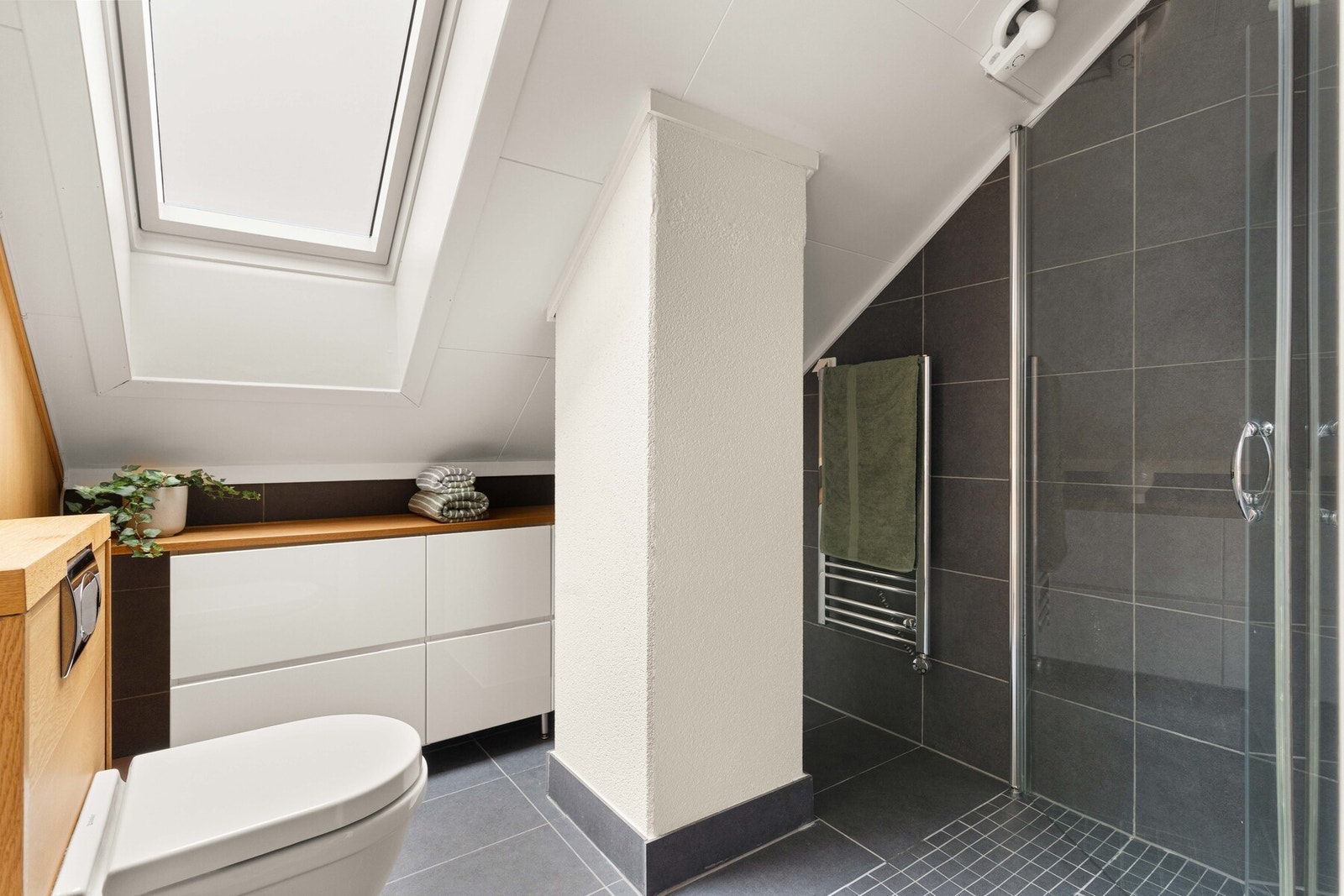 Dusj på gulv med innfellbare glassdører, vegghengt toalett og praktiske oppbevaringsløsninger gjør badet funksjonelt. Galleribilde