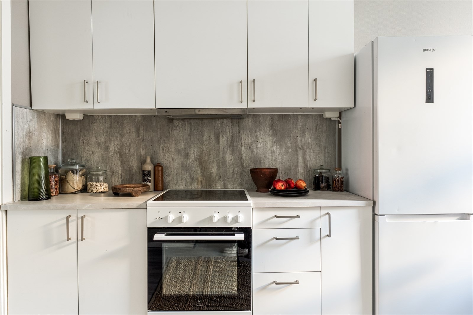 Enkel kjøkkeninnredning med slette fronter, plater og belysning over laminat benkeplate med nedfelt oppvaskkum. Galleribilde